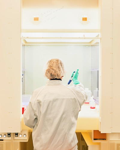 Aufnahme einer Laborantin, die in Kittel und Haube mit einer Pipette arbeitet.