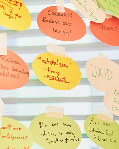 Zettel mit Ergebnissen aus einem Brainstorming hängen an einer Glasfläche in einer Universität während eines Workshops zum Unternehmertum.