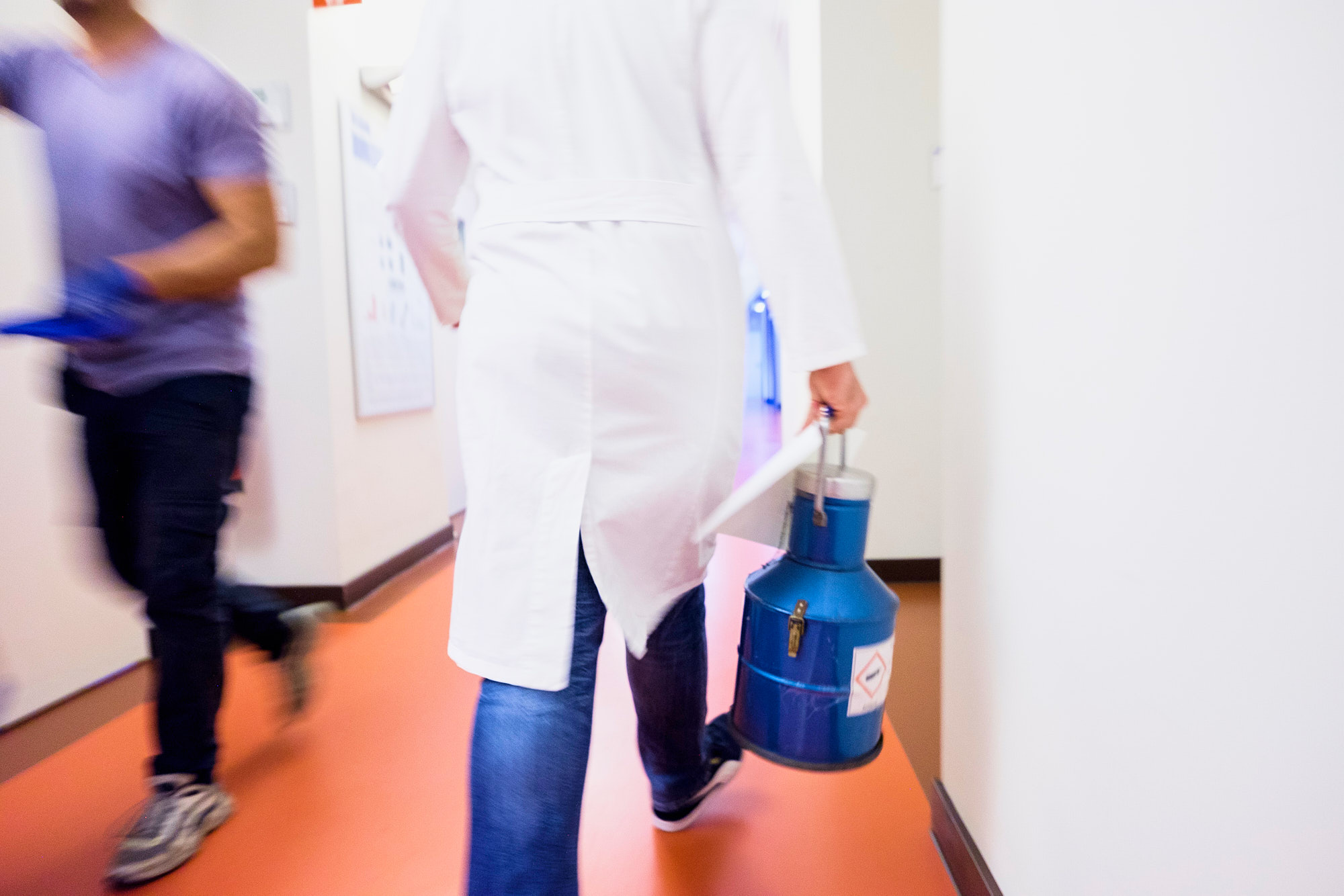 Ein Wissenschaftler trägt einen Kanister mit flüssigem Stickstoff durch den Gang einer Universität.