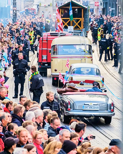 Pressefotografie von einem Straßenumzug, auf dem gerade Oldtimer an den Menschen vorbeifahren.