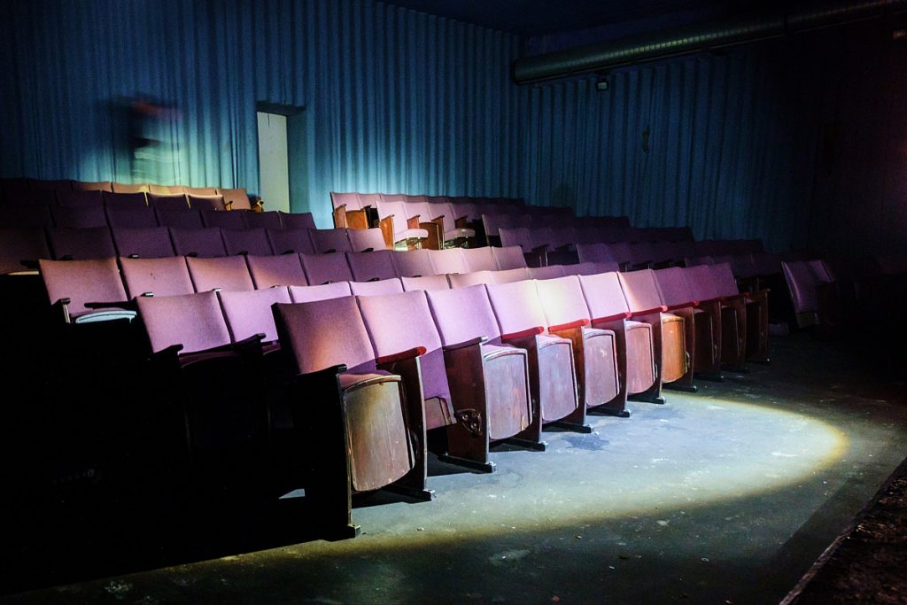 Dokumentarfotografie eines verlassenen Kinosaals, der von einer Taschenlampe angeleuchtet wird.